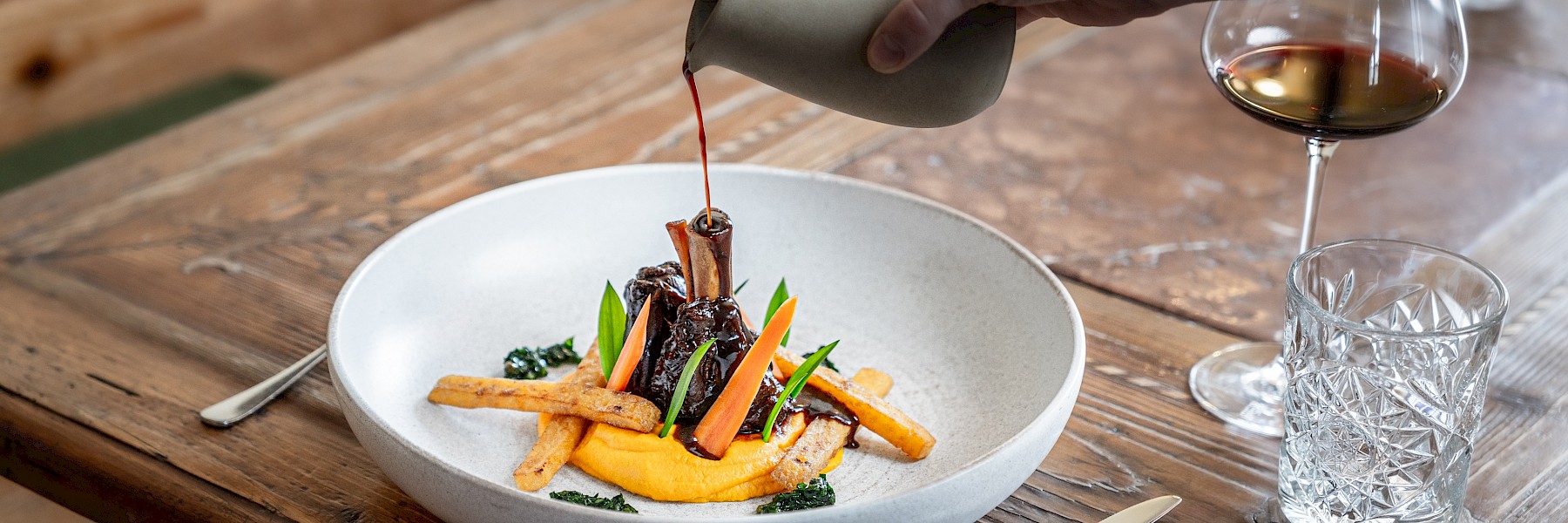 Die Aufnahme zeigt das elegante Eingangsschild des „Rosewood Munich“, montiert an einer Fassade aus rustikalem Sandstein. Die goldenen, stilvoll in das dunkle Metallschild eingelassenen Buchstaben heben sich kontrastreich von der hellen Natursteinwand ab und unterstreichen den luxuriösen Charakter des Gebäudes. Die Architektur kombiniert klassische Elemente mit moderner Ästhetik, was dem Hotel einen exklusiven und zugleich einladenden Auftritt verleiht. Im Vordergrund sind gepflegte Pflanzgefäße zu erkennen, die den gehobenen Stil zusätzlich unterstreichen. Das Bild vermittelt einen ersten Eindruck von Eleganz, Klasse und hochwertigem Design mitten im Herzen Münchens.