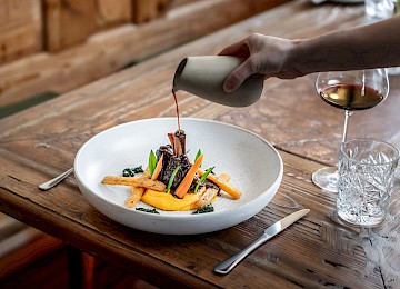 Die Aufnahme zeigt das elegante Eingangsschild des „Rosewood Munich“, montiert an einer Fassade aus rustikalem Sandstein. Die goldenen, stilvoll in das dunkle Metallschild eingelassenen Buchstaben heben sich kontrastreich von der hellen Natursteinwand ab und unterstreichen den luxuriösen Charakter des Gebäudes. Die Architektur kombiniert klassische Elemente mit moderner Ästhetik, was dem Hotel einen exklusiven und zugleich einladenden Auftritt verleiht. Im Vordergrund sind gepflegte Pflanzgefäße zu erkennen, die den gehobenen Stil zusätzlich unterstreichen. Das Bild vermittelt einen ersten Eindruck von Eleganz, Klasse und hochwertigem Design mitten im Herzen Münchens.