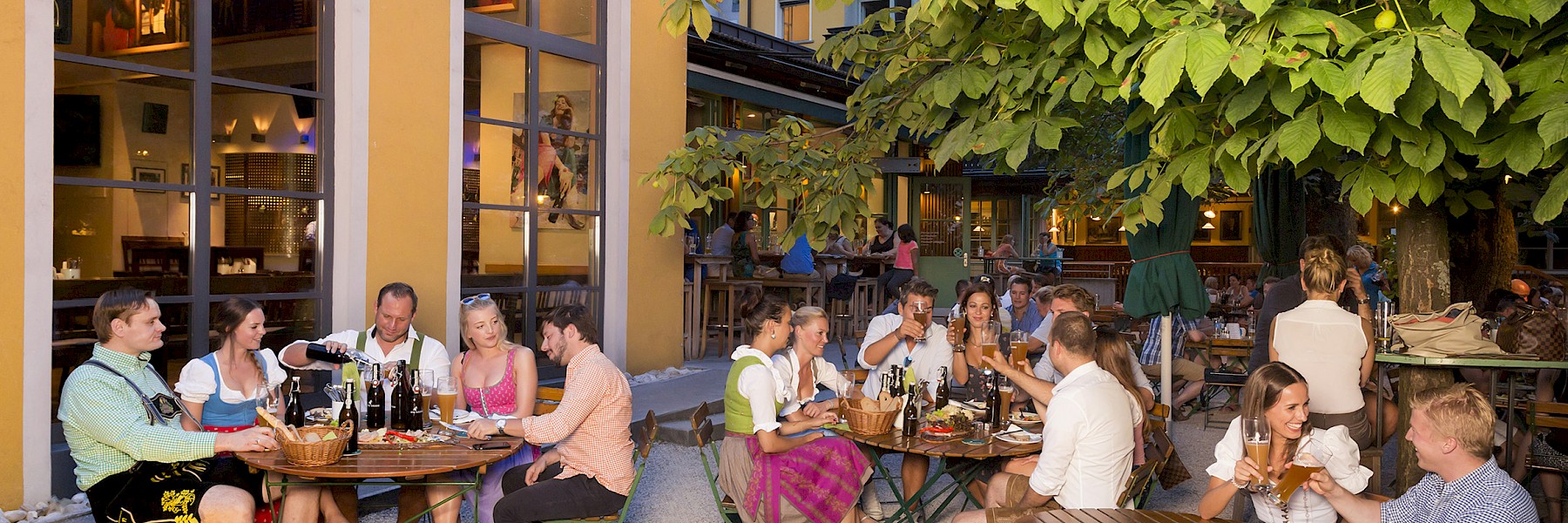Die Aufnahme zeigt das elegante Eingangsschild des „Rosewood Munich“, montiert an einer Fassade aus rustikalem Sandstein. Die goldenen, stilvoll in das dunkle Metallschild eingelassenen Buchstaben heben sich kontrastreich von der hellen Natursteinwand ab und unterstreichen den luxuriösen Charakter des Gebäudes. Die Architektur kombiniert klassische Elemente mit moderner Ästhetik, was dem Hotel einen exklusiven und zugleich einladenden Auftritt verleiht. Im Vordergrund sind gepflegte Pflanzgefäße zu erkennen, die den gehobenen Stil zusätzlich unterstreichen. Das Bild vermittelt einen ersten Eindruck von Eleganz, Klasse und hochwertigem Design mitten im Herzen Münchens.